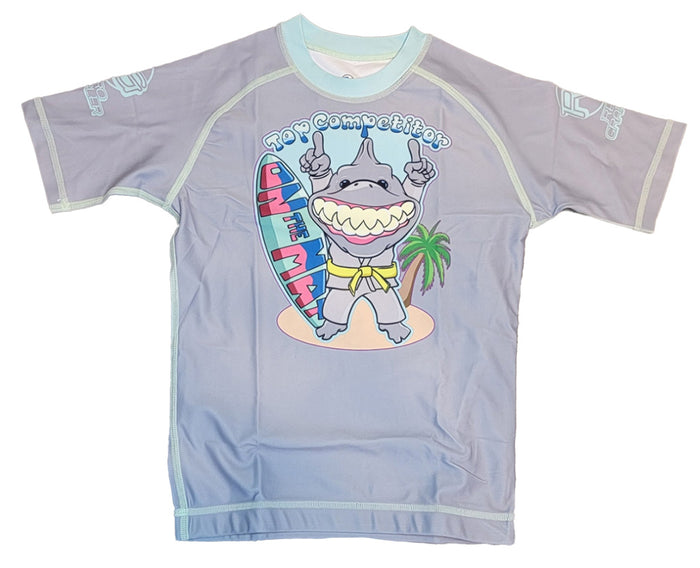 The Retro Grappler Youth - Competition Shark shirt is a light purple, fitted short sleeve featuring a cartoon shark in sunglasses flashing two fingers beside a surfboard and palm tree, with Top Competition above.