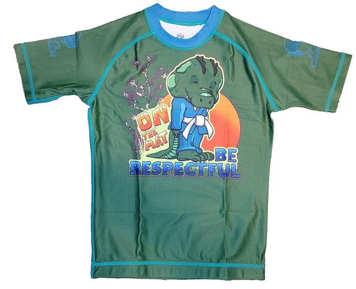 The Retro Grappler Youth - Respectful Gator rash guard features green short sleeves, blue trim, a cartoon gator in a gi with ON THE MAT BE RESPECTFUL text, and sleeve accents. Made from comfy polyester-spandex four-way stretch fabric.