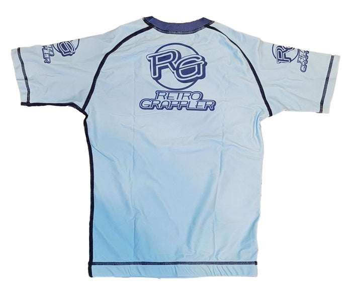 The Youth - Take Down Tiger by Retro Grappler is a light blue short-sleeve athletic shirt with dark blue seams, fitted design, and four-way stretch fabric. RETRO GRAPPLER and the RG logo are boldly printed on the back in blue letters.